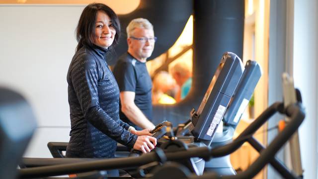 Mann und Frau laufen auf Laufband und blicken in die Kamera