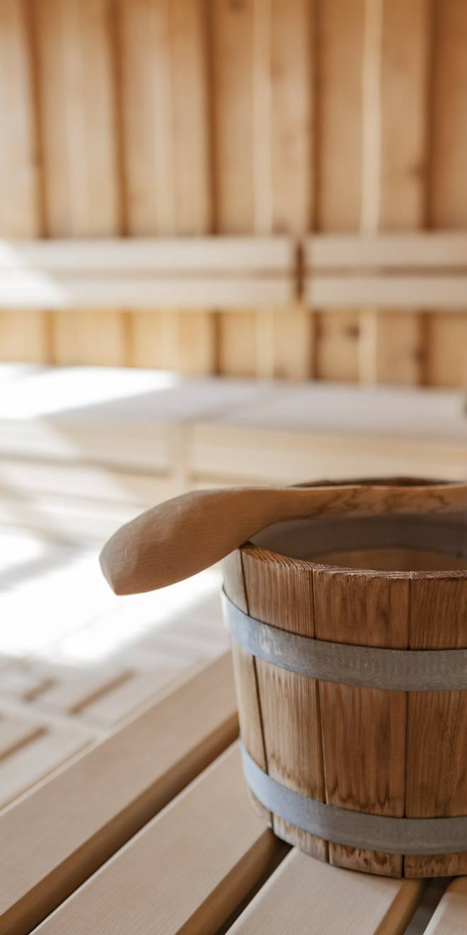 Sauna im Wellnesshotel in Thüringen mit hellem Holzinterieur, Aufgusseimer und Saunakellen auf der Bank.