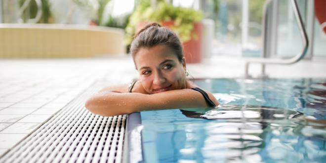 Frau im Erlebnisbecken lehnt am Beckenrand.